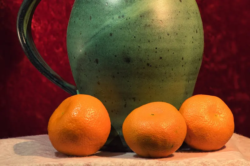 Jarra de cerámica junto a tres naranjas