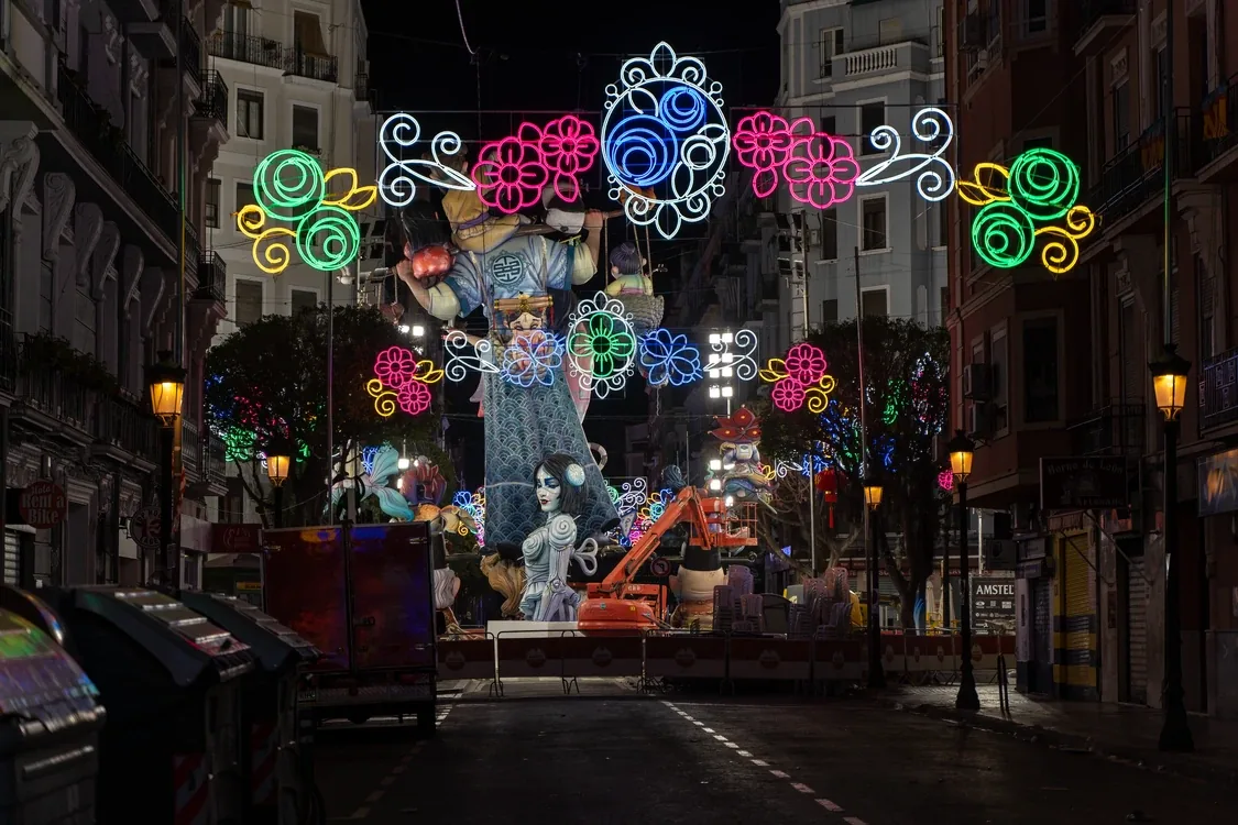 Falla iluminada de noche en una calle de Valencia, con arcos de luces de colores