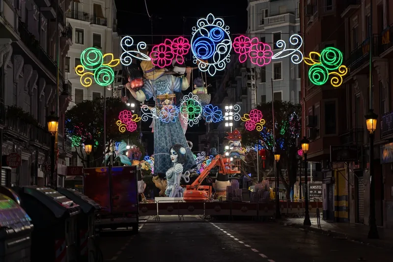 Falla iluminada de noche en una calle de Valencia, con arcos de luces de colores
