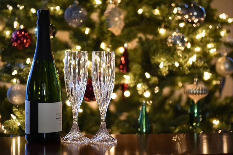 Botella de cava y dos copas de cristal delante de un árbol de Navidad iluminado