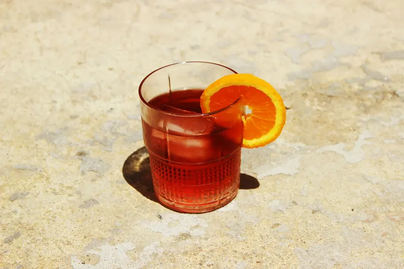 Vaso de vermut rojo con hielo y una rodaja de naranja al sol