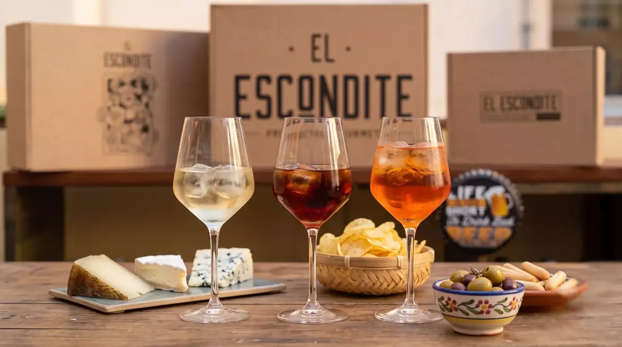 Vino blanco, vermut y spritz con quesos, patatas y aceitunas delante de las cajas regalo de El Escondite